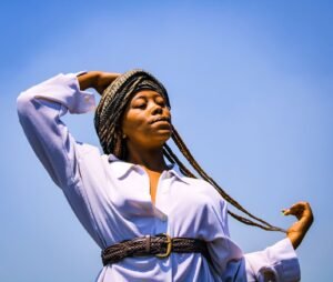 Portrait of a fashionable woman with braids in a white dress under a clear sky.