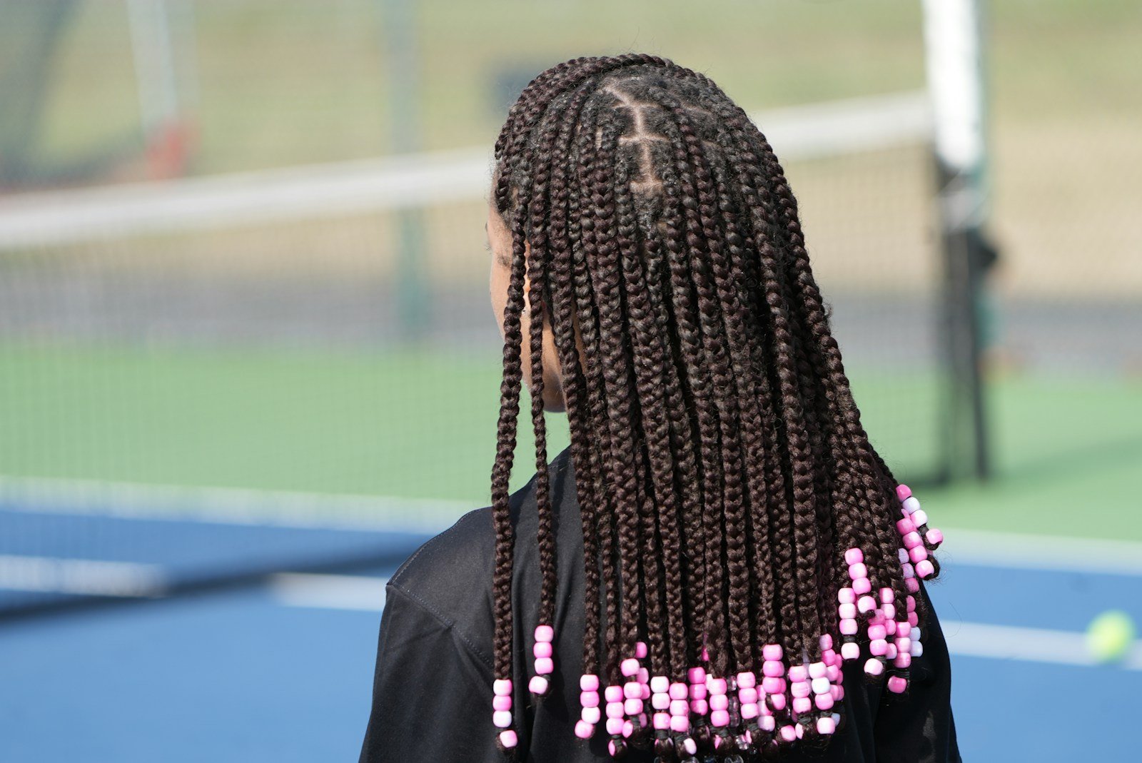 a woman with long box braids on a tennis court